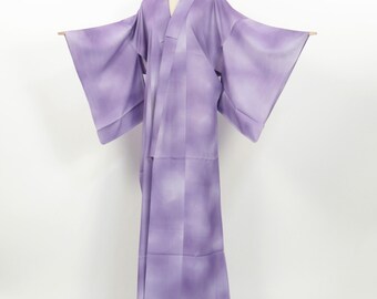 May include: A light purple kimono with a gradient pattern, displayed on a mannequin. The kimono features wide sleeves and a V-neck design. The fabric has a subtle, textured appearance, and the garment is floor-length.