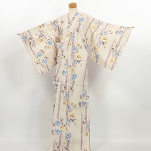 May include: Cream-colored kimono with vertical lavender stripes and floral patterns in blue and yellow. The kimono has wide sleeves and is displayed on a mannequin. The floral design is repeated across the garment.