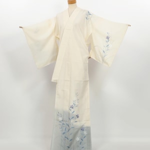 May include: Cream-coloured Japanese kimono with a floral design in shades of blue and white. The kimono is displayed on a mannequin, showcasing its wide sleeves and floor-length skirt. The floral pattern is concentrated on the sleeves and the lower portion of the garment.