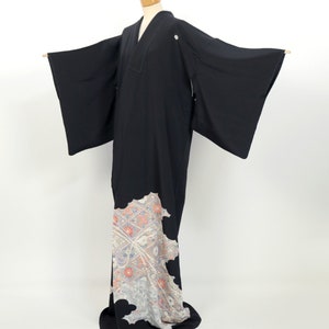 May include: A black kimono with a white and pink floral pattern on the bottom hem. The kimono has long sleeves and a V-neck.