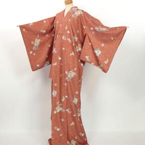 May include: A rust-colored kimono with a floral pattern. The kimono has a traditional Japanese design and is made of a soft, flowing fabric.