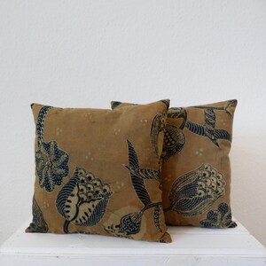 Könnte beinhalten: Zwei dekorative Kissen mit Blumenmuster. Die Kissen sind aus braunem Stoff mit einem blauen und weißen Blumendesign. Die Kissen liegen auf einer weißen Oberfläche.