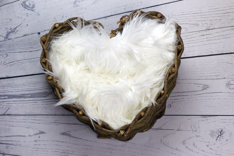 May include: A heart-shaped wicker basket filled with white faux fur, ideal for newborn photography props.