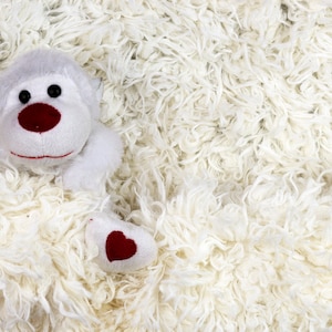 May include: A white plush monkey toy with red heart-shaped details, partially hidden in a white fluffy rug.