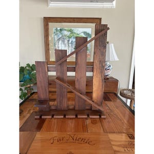 May include: A handcrafted wooden wine rack with a dark brown finish. The rack features vertical supports, angled bottle holders, and a base for holding wine glasses. The design is rustic and elegant, suitable for displaying wine bottles.