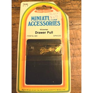 May include: A package of miniature Victorian drawer pulls. The package has a colorful rainbow design with the words "MINIATURE ACCESSORIES" and "Drawer Pull". The package contains 8 pieces.