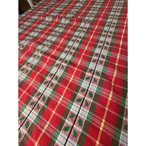 May include: Red plaid tablecloth with green, yellow, and white stripes. The pattern includes holly leaf and berry accents. The fabric is a festive design, suitable for holiday or seasonal decor.
