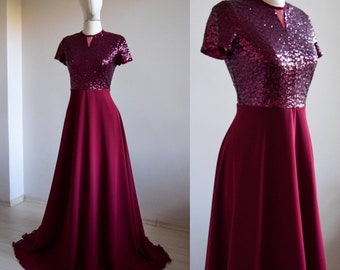 May include: A burgundy maxi dress with a sequined bodice and a flowing skirt. The dress has a scoop neckline and short sleeves.