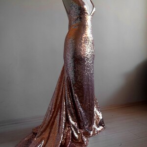 Pu&ograve; includere: Un abito da sera in paillettes color oro rosa con scollo a V e una lunga coda.