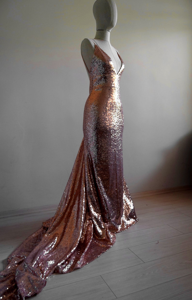 Pu&ograve; includere: Un abito da sera in paillettes color oro rosa con scollo a V e una lunga coda.