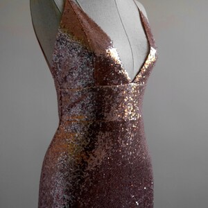 Pu&ograve; includere: Un abito senza maniche in paillettes color oro rosa con scollo a V profondo.