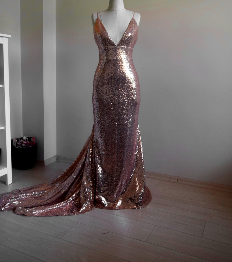 Pu&ograve; includere: Un abito da sera di paillettes color oro rosa con scollo a V e una lunga coda.