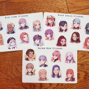 May include: Three sheets of stickers featuring anime-style characters. The first sheet is labeled "Blue Lions Stickers" and features 9 characters with blue, pink, and white accents. The second sheet is labeled "Black Eagles Stickers" and features 9 characters with black, red, and white accents. The third sheet is labeled "Golden Deer Stickers" and features 9 characters with gold, pink, and white accents.