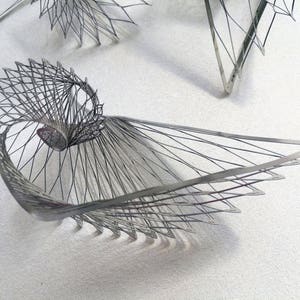May include: A silver metal sculpture with a geometric design. The sculpture is made of thin wires that are woven together to create a complex pattern.