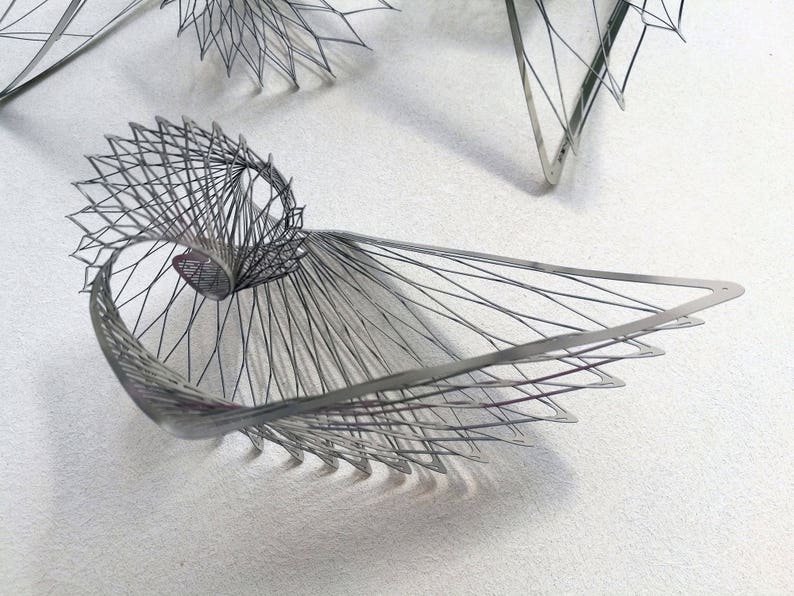 May include: A silver metal sculpture with a geometric design. The sculpture is made of thin wires that are woven together to create a complex pattern.