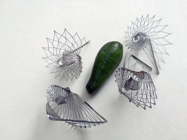 May include: Five wire sculptures in the shape of a spiral, with a green avocado in the center.