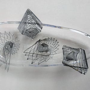 Puede incluir: Un cuenco de vidrio transparente con cuatro esculturas de alambre negro en su interior. Las esculturas son de diseño geométrico y abstracto.