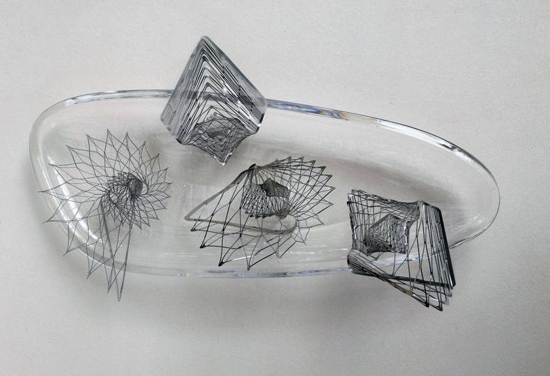 May include: A clear glass bowl with four black wire sculptures inside. The sculptures are geometric and abstract in design.