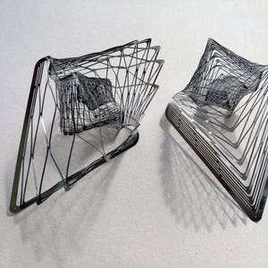 May include: Two silver metal sculptures with a geometric design. The sculptures are made of thin metal strips that are woven together to create a three-dimensional shape.