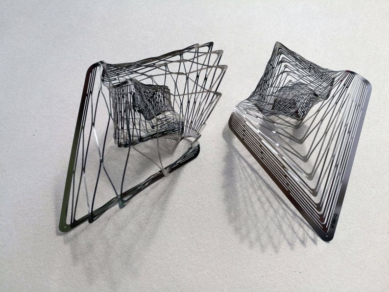 May include: Two silver metal sculptures with a geometric design. The sculptures are made of thin metal strips that are woven together to create a three-dimensional shape.