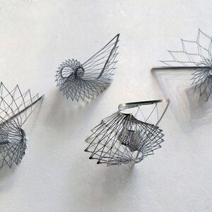 May include: Four silver wire sculptures in the shape of a spiral. The sculptures are arranged on a white surface.