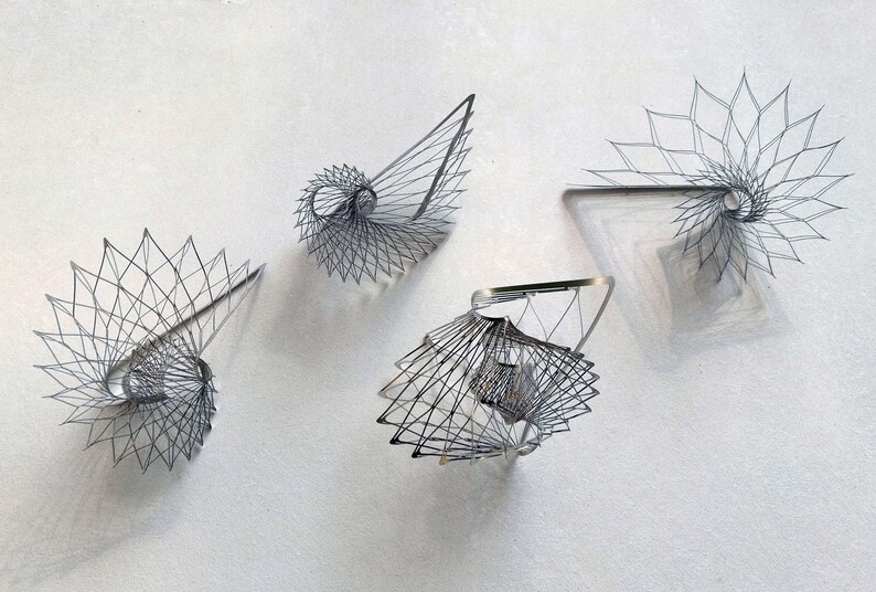 May include: Four silver wire sculptures in the shape of a spiral. The sculptures are arranged on a white surface.