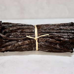 May include: A bundle of dried vanilla beans tied together with twine. The beans are dark brown and have a glossy finish.
