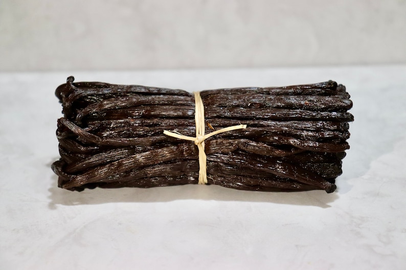May include: A bundle of dried vanilla beans tied together with twine. The beans are dark brown and have a glossy finish.