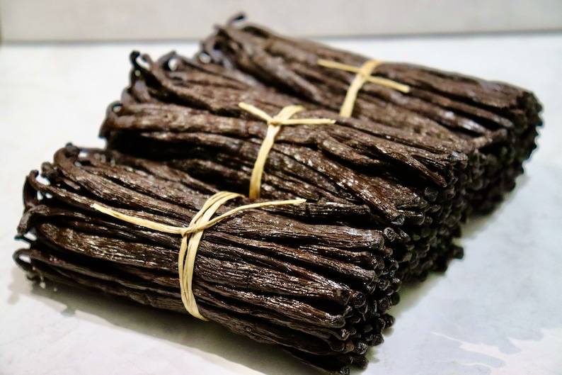 May include: Three bundles of dried vanilla beans tied with twine. The beans are dark brown and have a glossy finish.