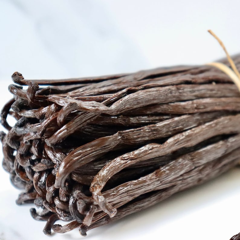 May include: A bundle of dried vanilla beans, tied together with twine. The beans are dark brown and have a glossy finish.