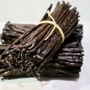 May include: A bundle of dried vanilla beans tied together with a string. The beans are dark brown and have a glossy finish.