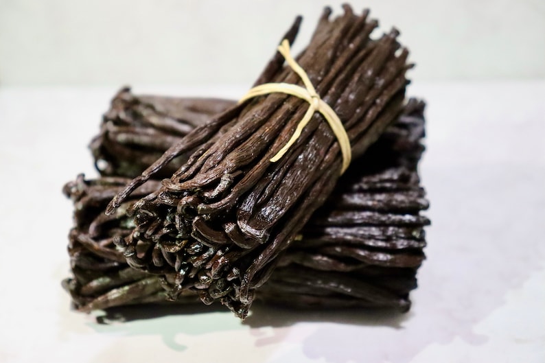 May include: A bundle of dried vanilla beans tied together with a string. The beans are dark brown and have a glossy finish.