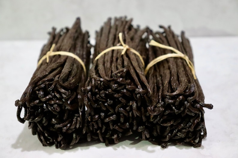 May include: Three bundles of dried vanilla beans tied with twine. The beans are dark brown and have a glossy finish.