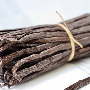 May include: A bundle of dried vanilla beans tied together with twine. The beans are dark brown and have a glossy finish.