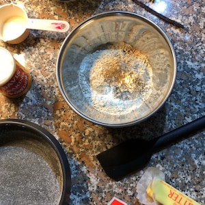 May include: A close-up of a kitchen counter with baking ingredients, including flour, sugar, butter, and vanilla beans. There is also a baking pan and a bowl of cream.