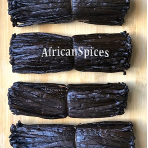 May include: Four bundles of dried vanilla beans tied together with twine, arranged on a wooden surface. The bundles are dark brown in color and have a glossy finish. The text "AfricanSpices" is visible in the center of the image.