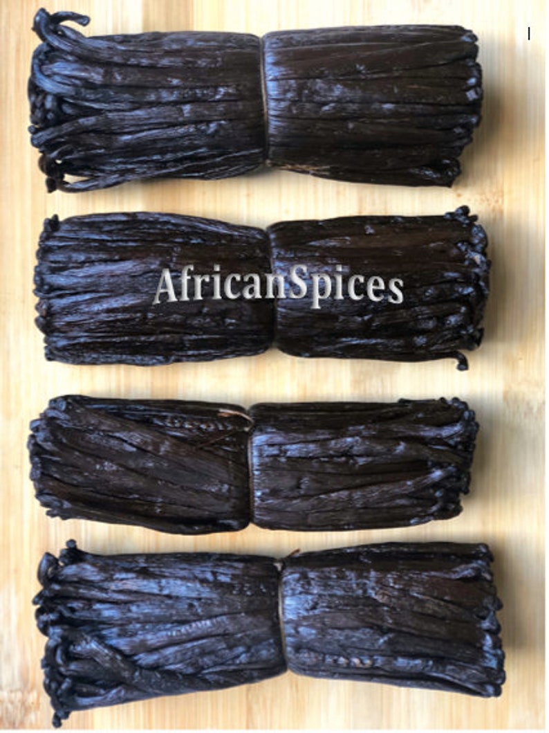 May include: Four bundles of dried vanilla beans tied together with twine, arranged on a wooden surface. The bundles are dark brown in color and have a glossy finish. The text "AfricanSpices" is visible in the center of the image.