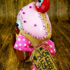May include: A pink and brown felt cupcake with a red felt cherry on top. The cupcake has pink polka dots and a brown felt base. It has a tag that says "Happy Birthday" with a heart and the words "Rush Bind".