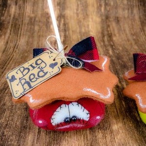 May include: Two felt ornaments shaped like houses with a red and black checked bow and a brown tag. The tag on the left ornament says "Big Red".