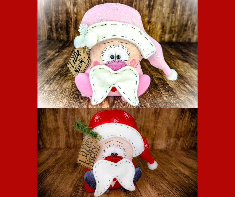 May include: Two plush gnome dolls with stitched details, one in pink and one in red. Each features a floppy hat with white snowflake embroidery, a large white moustache, and a tan tag attached to the side that reads Little Nicky in black ink.