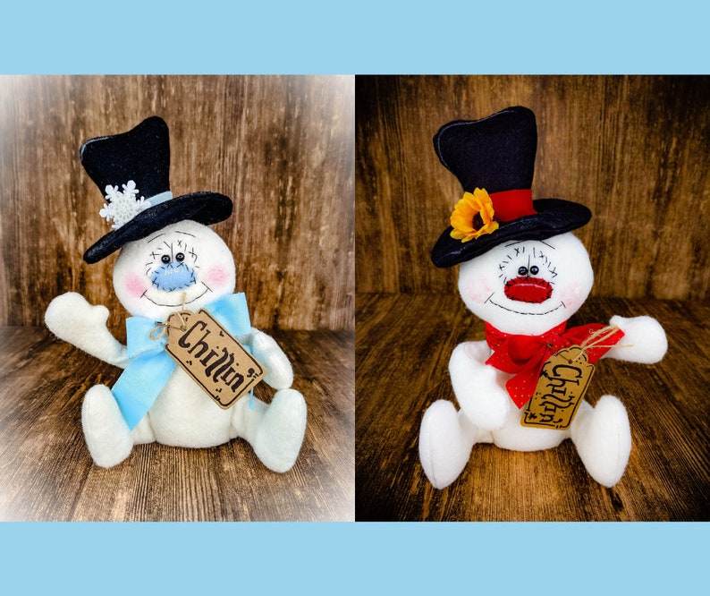 Puede incluir: Dos figuras de mu&ntilde;eco de nieve blancas con sombreros negros, una con un lazo azul y la otra con un lazo rojo. Ambos mu&ntilde;ecos de nieve tienen una etiqueta marr&oacute;n que dice "Chillin".