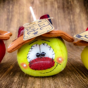 May include: Three handmade plush ornaments shaped like apples with stitched details. Each apple has a different colour and a tag with a different word on it. The words are "Fall", "Joy", and "Gather".
