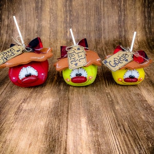 May include: Three handmade fabric apples with stick stems and brown paper tags. The apples are red, yellow, and green. The tags read "Big Red", "Lil'  Tater", and "Golden".
