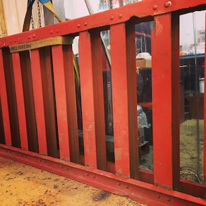 May include: A red metal loading ramp with a weight limit of 6400 lbs. The ramp has a series of vertical bars and a metal plate at the bottom.
