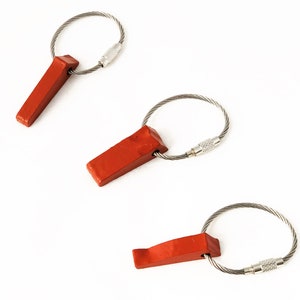 May include: Three red wooden wedges attached to silver steel key rings. The wedges are rectangular with a beveled edge. The key rings are made of twisted steel wire and have a screw clasp.