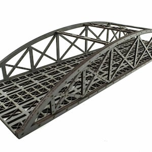 May include: A gray metal bridge model with a lattice design. The bridge has a curved arch and is made of metal bars and plates.