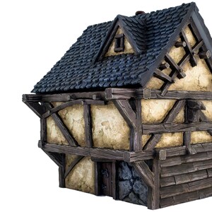 May include: A miniature wooden house with a dark blue shingled roof, a small window, and a stone foundation. The house has a half-timbered facade with exposed wooden beams and a weathered, cream-colored plaster.