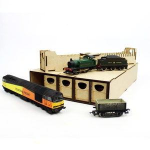 Könnte beinhalten: Eine Sammlung von Modelleisenbahnen und ein Holzschuppen. Die Züge umfassen eine Colas Rail Freight Lokomotive, eine grüne Dampflok, einen Kohlewagen und einen grauen Güterwagen. Der Schuppen hat mehrere Buchten.