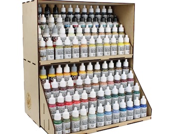Op de afbeelding: Een houten verfstandaard met drie planken, met rijen kleine glazen flesjes met acrylverf. De flesjes zijn gelabeld met "Model Color" en zijn gerangschikt in een regenboog van kleuren.