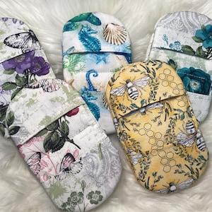 May include: Five fabric pouches with different designs. The pouches are all oval shaped and have a flap that closes with a velcro strap. The designs include butterflies, seahorses, bees, and flowers.
